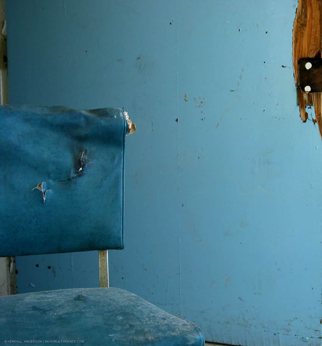 A blue dusty chair rests against a blue door.