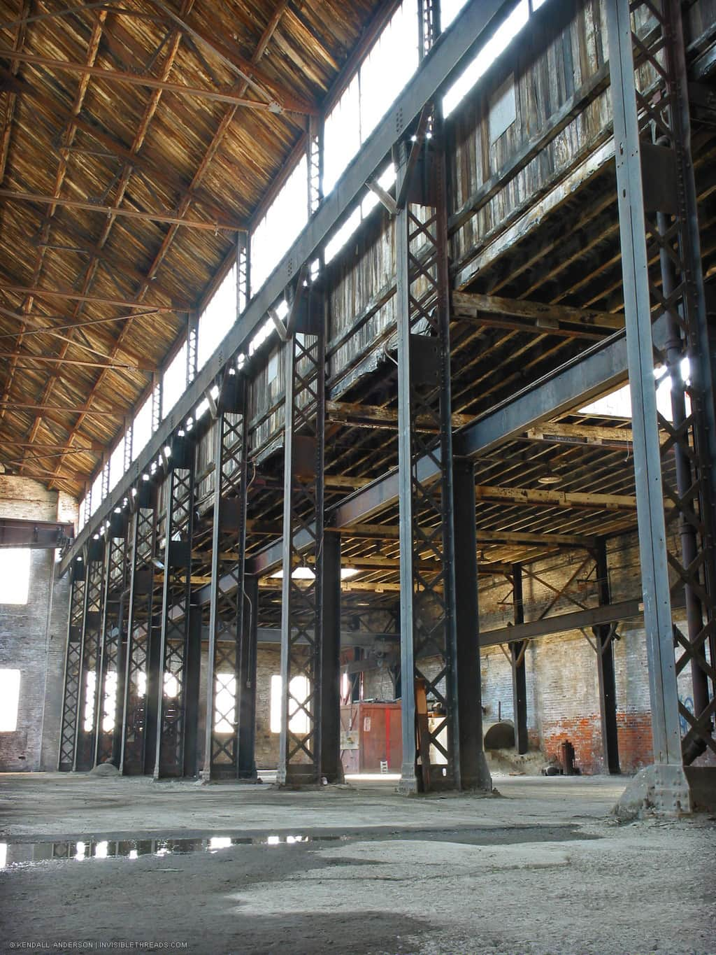 Interior of old empty industrial warehouse with steel columns. Looking up at skylights and wood roof decking.