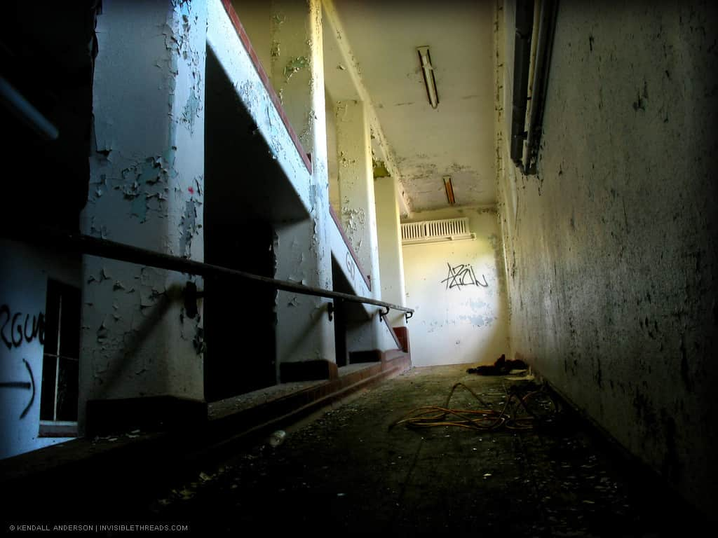 A long ramp leads down from the ground floor to the basement. Debris is on the ground, and graffiti on the walls.