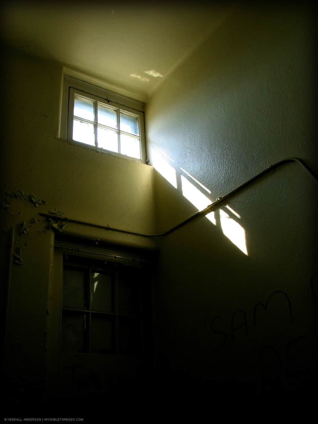 Inside a dark room with yellow walls, a small skylight above the closed door allows light in near the ceiling.