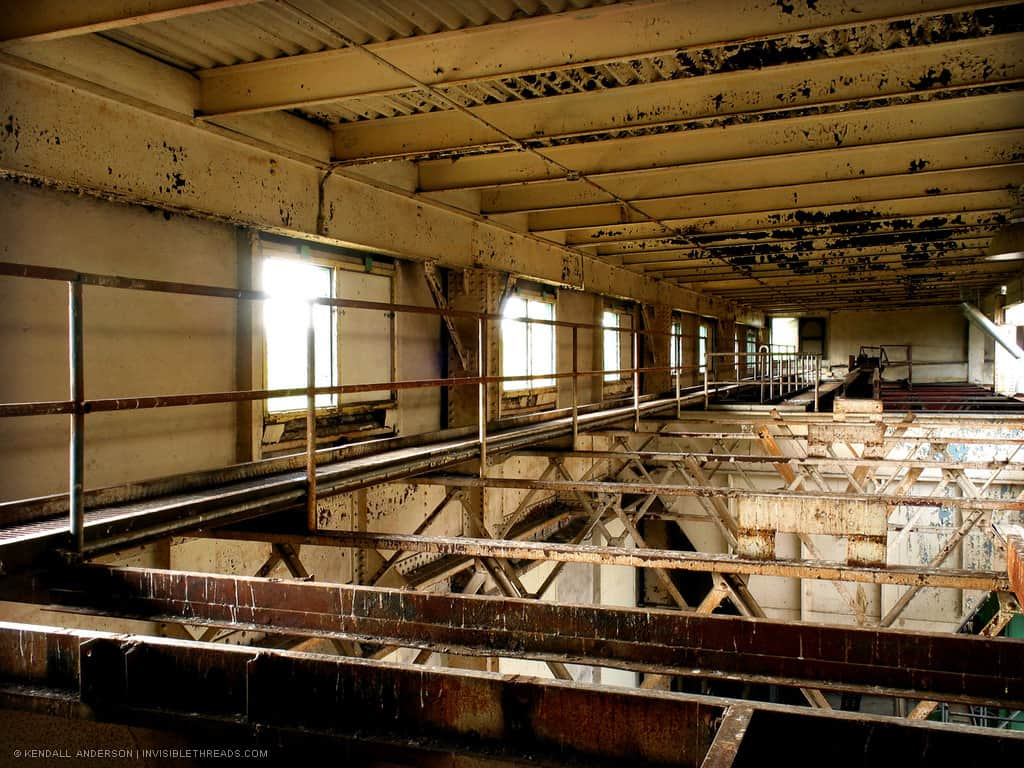 A catwalk runs along the window-lined wall in the attic area of a mechanical room. Steel beams are seen above and below.