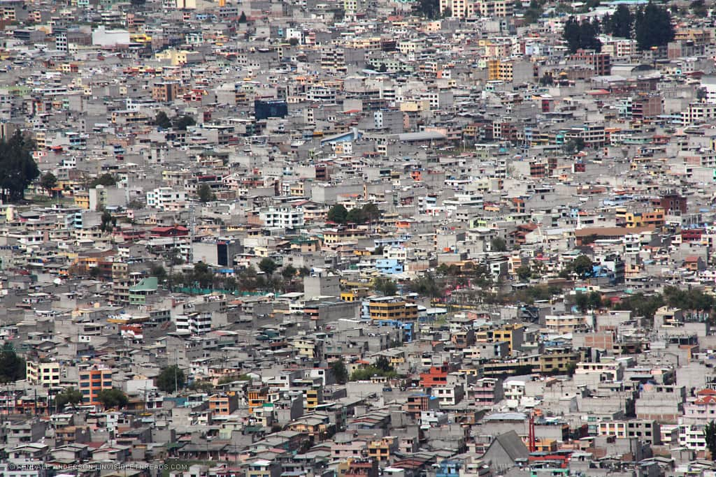 A valley hillside is completely covered by a city of hundreds of concrete and plaster 3 and 4-storey buildings. Virtually no vegetation can be seen. The entire surface is covered by a dense built environment.