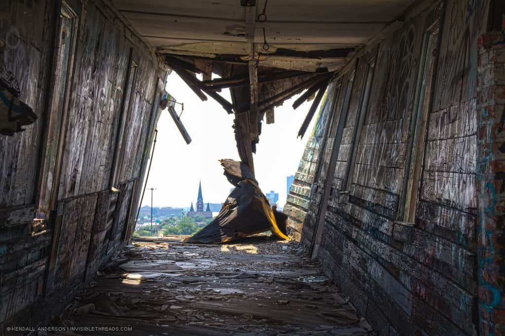 Dark twisted collapsing hallway, rubble floor, graffiti walls, with exterior view towards a church in the distance