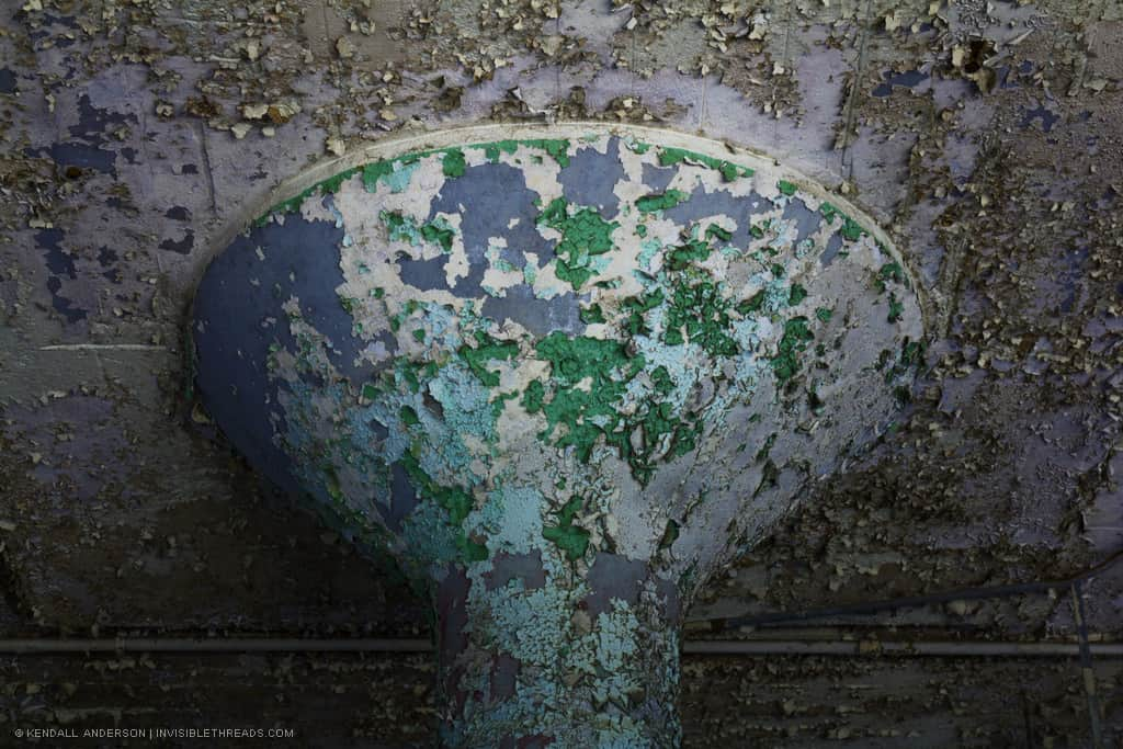 Top of a painted concrete column inside a warehouse. All of the paint is flaking off showing previous colors through multiple layers.